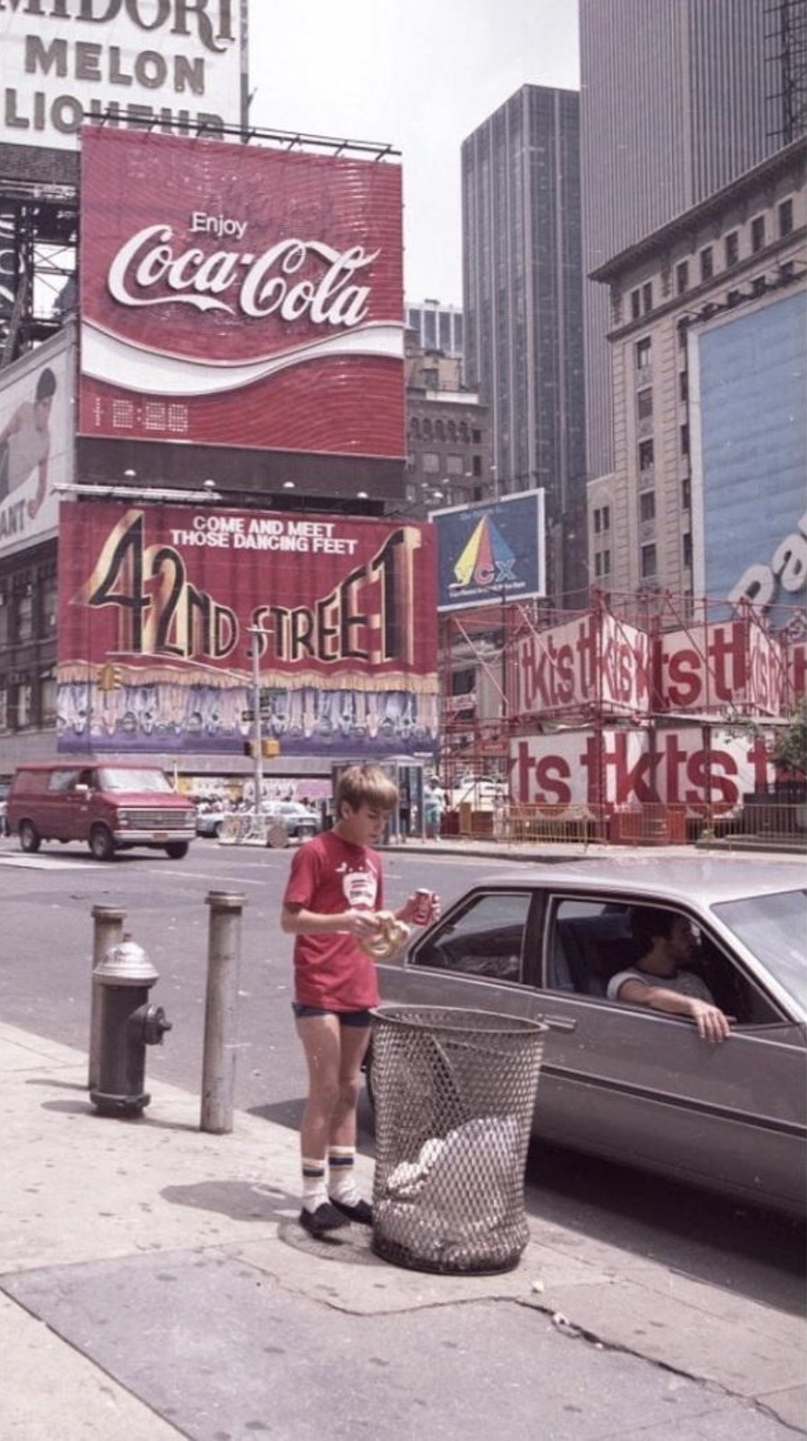 Boy holding a Coke can in front of a Coca-Cola billboard in Times Square, NY, 1970s